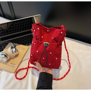 Detail of red floral pleated crossbody bag with woven rope strap and magnetic snap closure