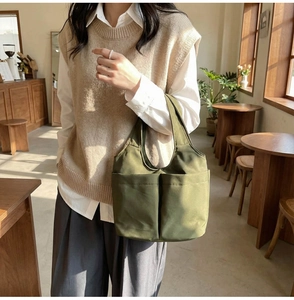 Dettaglio della borsa tote in tela verde militare con due tasche frontali e manici robusti