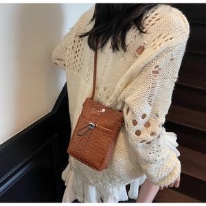 Detail of a brown woven crossbody phone bag with adjustable drawstrings and metal buckle