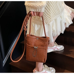 Close-up of brown textured crossbody phone bag with woven strap on a female model