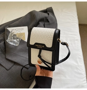Detail of woven leather crossbody bag with black and white contrast and metal pendant