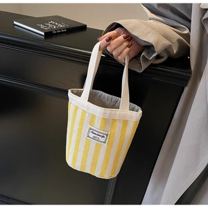 Detailed shot of yellow and cream striped canvas tote with brand label and top handles