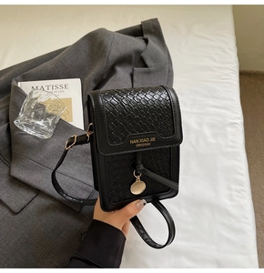 Detail of black woven pattern crossbody bag with gold logo and stylish accessories