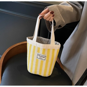 Close-up of yellow striped canvas tote with brand label on a dark background