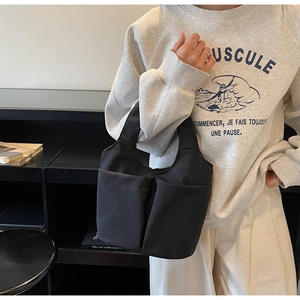 Dettaglio della borsa a secchiello nera in tessuto con ampie tasche frontali minimaliste