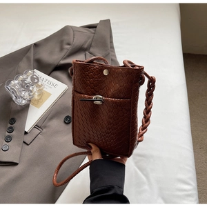 Detail of hand-held dark brown woven crossbody bag with metal twist lock and magnetic closure
