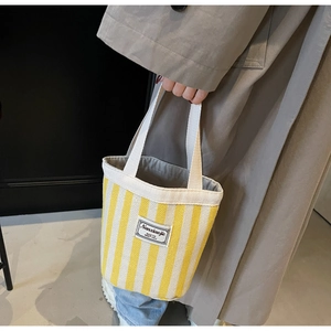 Detail of yellow and white striped canvas tote bag with woven brand label and sturdy handles