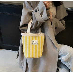 Detailed side view of yellow and white striped canvas bucket bag with Nanxiaojie logo