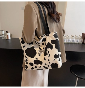 Detail of cow print corduroy tote bag with black straps and brand patch in a cafe