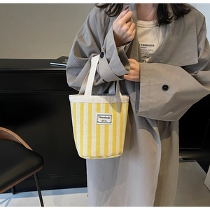 Detail of yellow and white striped canvas tote bag with woven handles and brand label