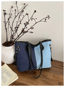 Detail of a large denim tote bag featuring tri-color stitching on a rustic wooden desk