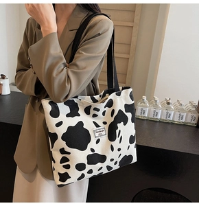 Detailed close-up of cow print corduroy tote bag with black canvas straps and logo patch