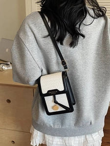 Fashionable woven crossbody bag in black and white leather with gold pendant detail