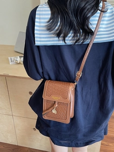 Stylish brown woven crossbody phone bag with leather texture and gold pendant detail