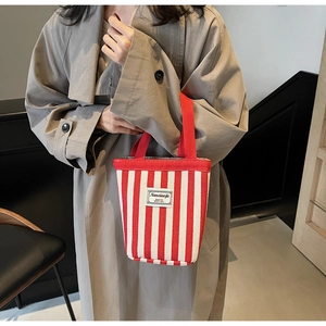 Detail of red and white striped canvas tote bag with woven label shown on a trench coat