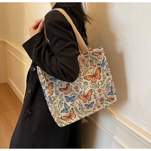 Detail of canvas tote bag with butterfly floral prints worn by a model in a black blazer