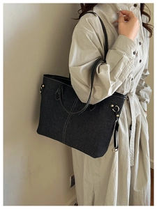 Detail of dark blue denim tote bag with white contrast stitching and gold metal ring hardware