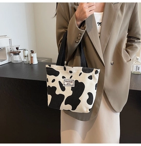 Close-up of cow print tote bag with woven handles and minimalist brand label detailing