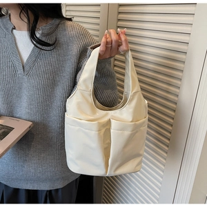 Dettaglio della borsa a secchiello color crema con ampie tasche esterne e stile minimalista