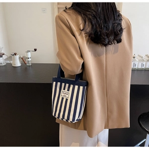 Detailed back view of a woman holding the striped canvas handbag in a modern cafe setting