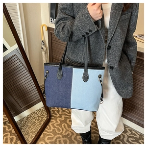 Close-up of contrast denim tote bag showing leather handles and gold metal hardware