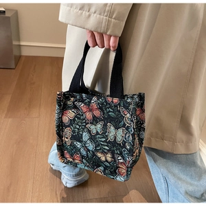 Detailed shot of dark green tote with colorful butterfly jacquard and black woven handles