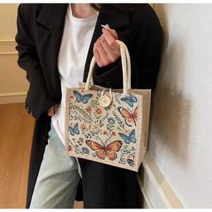 Detailed close-up of butterfly and floral embroidery on a linen handbag with rope handles
