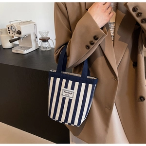 Detailed close-up of a blue and white striped canvas handbag with a woven navy handle