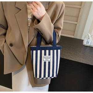 Detail of blue and white striped canvas bucket bag held by model wearing a brown blazer