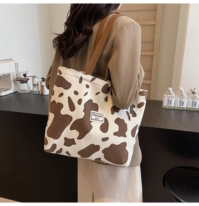 Detail view of cow print corduroy tote bag with woven shoulder strap and brand patch