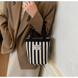 Detailed view of striped canvas bucket bag with woven label being carried by a model