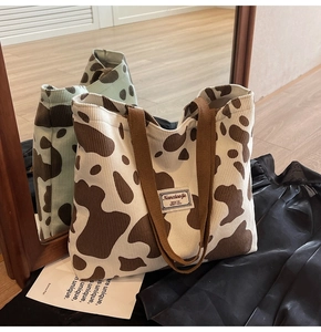 Detail of corduroy tote bag with brown cow pattern and branding on mirror background