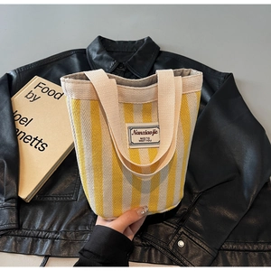 Detail of yellow striped canvas tote bag with woven handles and minimalist brand label