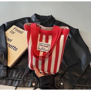 Detail shot of a red and white striped canvas tote bag resting on a black leather jacket