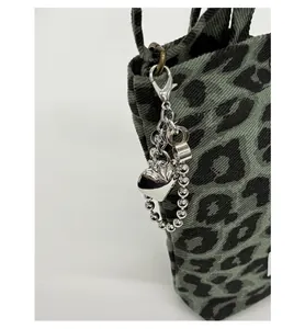 Close-up of detachable silver heart-shaped metal pendant on leopard print crossbody bag