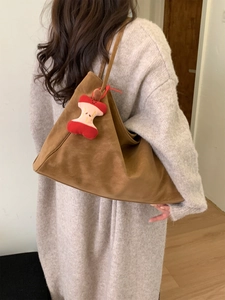 Large brown suede tote bag with cute apple core pendant worn by a model in soft light