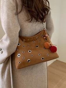 Retro brown suede shoulder bag with metal eyelets and colorful pompom charm on a model