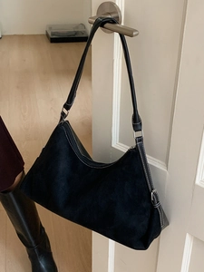 Grand sac hobo noir avec surpiqûres blanches contrastées suspendu à une poignée de porte