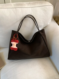 Large dark brown tote bag in matte suede finish with cute apple charm on a beige sofa