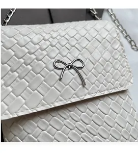 Close-up of white woven texture and silver metal bow decoration on a crossbody bag