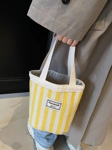 Fashionable yellow striped canvas tote bag held by a model in a casual lifestyle setting