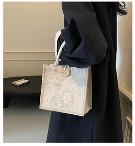Detail of beige square handbag featuring 3D floral embossing and woven rope handles
