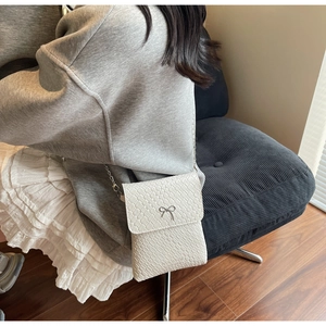 Detail view of woven texture and silver bow ornament on a beige crossbody bag