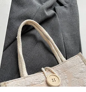 Close-up of beige jacquard handbag with floral texture, wooden button, and woven handles