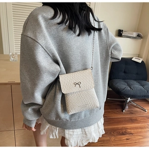 Detailed texture of white woven shoulder bag with metal bow and logo lettering