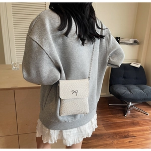 Macro detail of creamy white textured faux leather with silver bow buckle on small bag