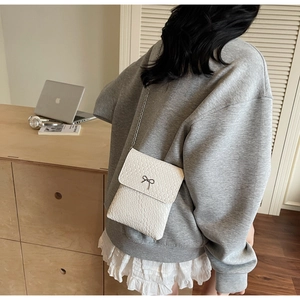 Close-up of white crocodile pattern shoulder bag with a metal bow and chain strap