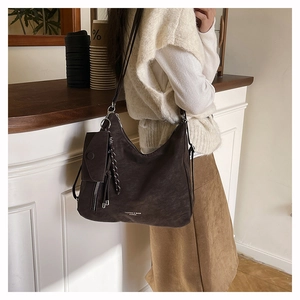 Detail der dunkelbraunen Hobo-Tasche aus Wildlederimitat mit Fashion-Schriftzug und Anhänger