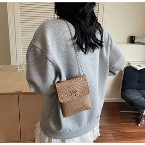 Close-up of brown woven texture PU leather crossbody bag with a black metal bow detail