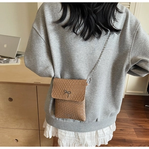 Detail of a brown woven leather crossbody bag with a metal bow and silver chain strap